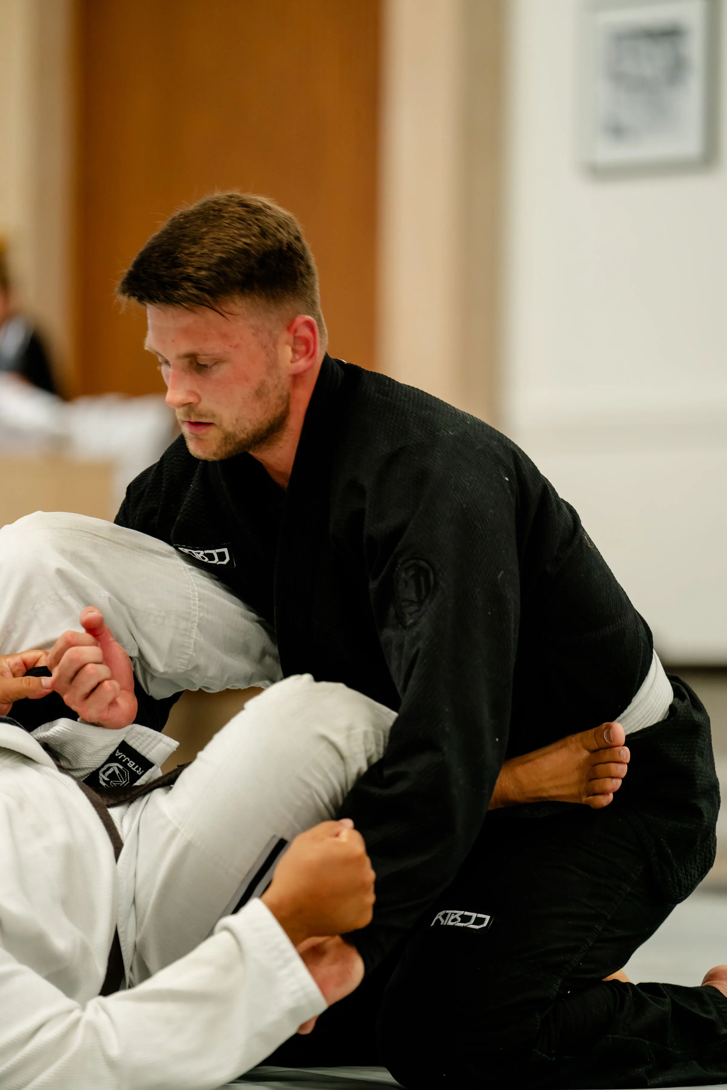 Adults Jiu Jitsu class at RT Beachside: the instructor in a black Gi guiding a student through a guard pass