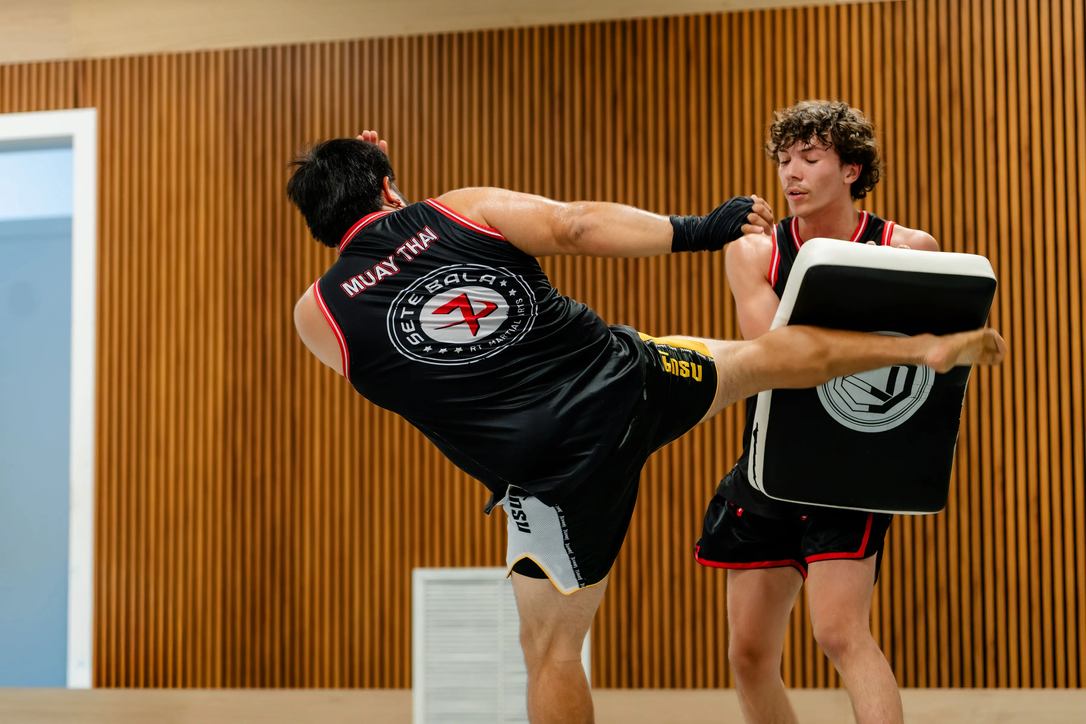 Adults Muay Thai class at RT Beachside: a student lands a high kick on the pad his training partner is holding