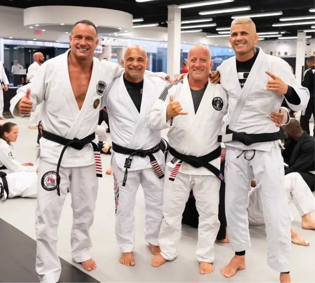 Four black belts in white Gis side by side on the mats at RT Headquarters