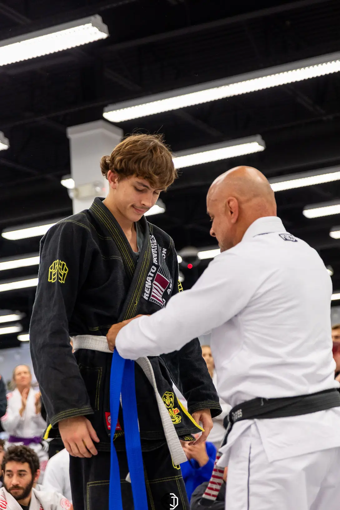 Master Renato Tavares tying a new blue belt on a smiling teen at RT Headquarters