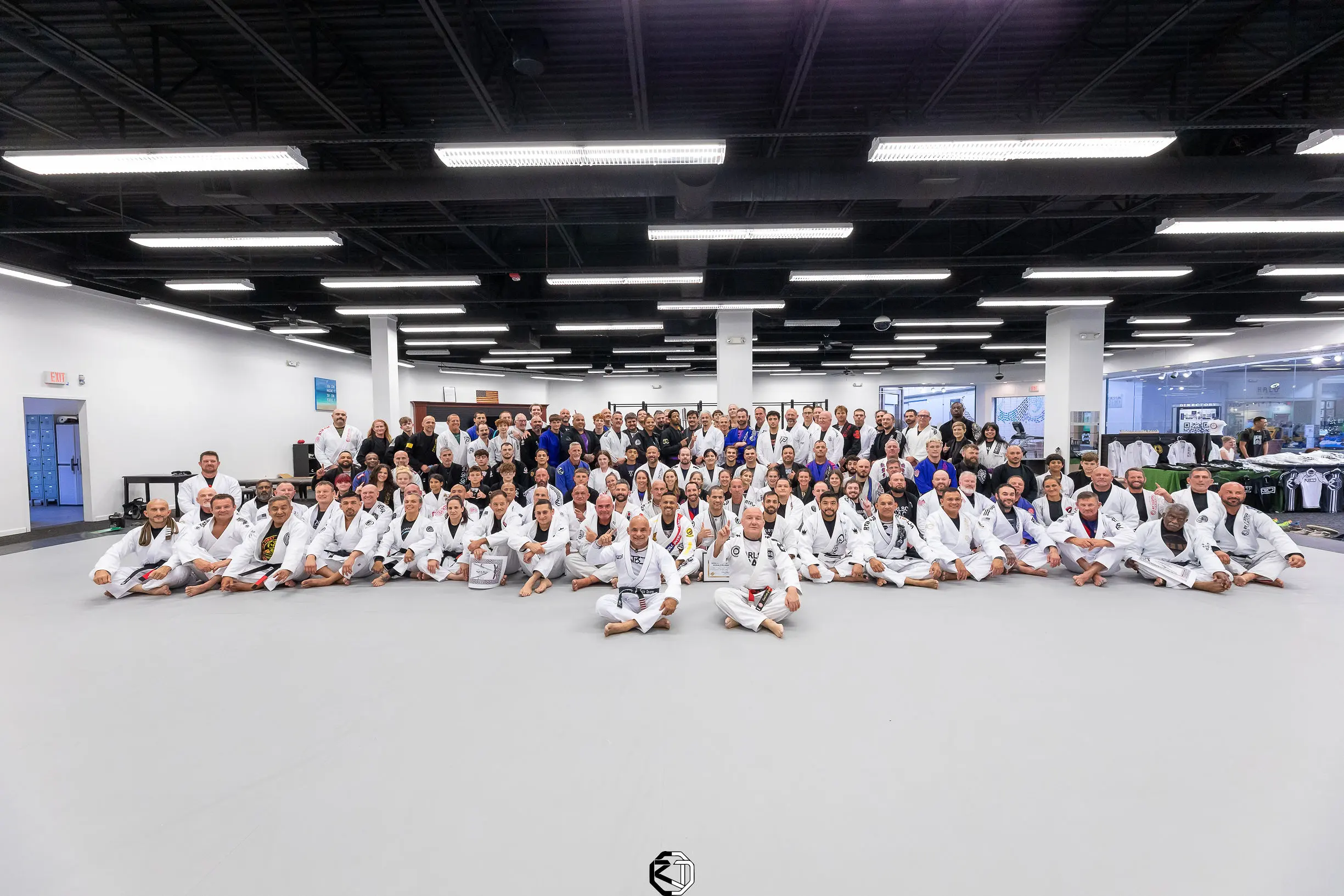 The whole academy on the mats at RT Headquarters: kids, teens and adults in white Gis, sitting together for the group photo after a seminar