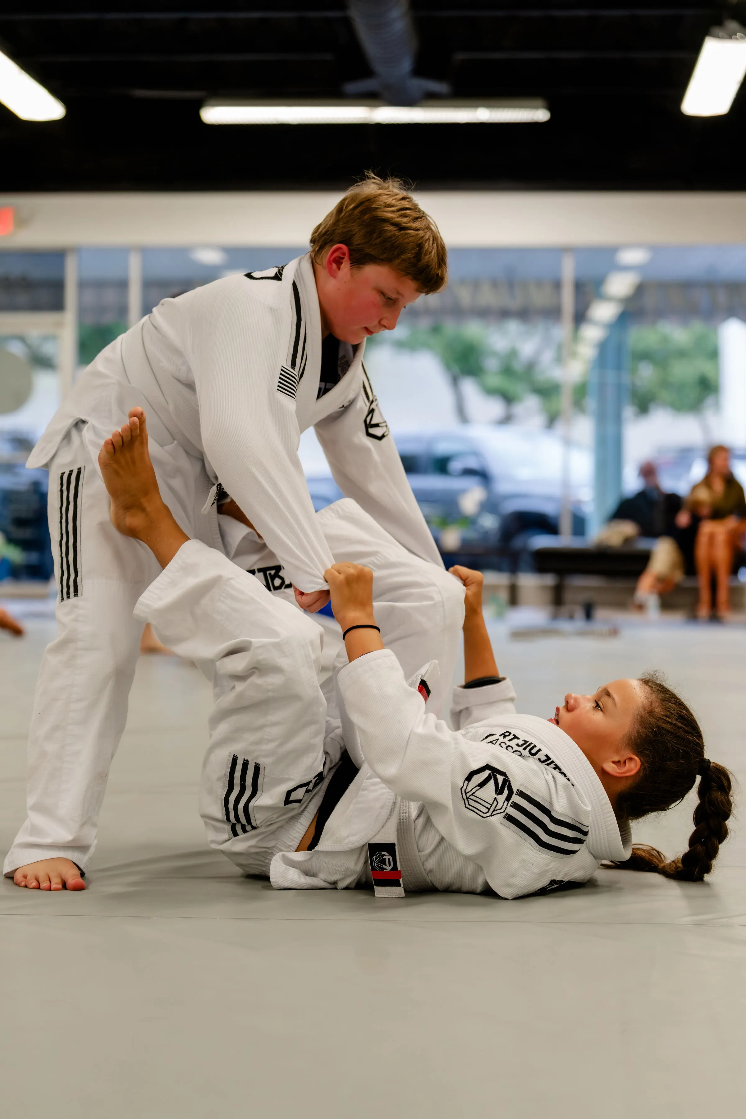 Kids Jiu Jitsu class at RT Beachside: two students in white Gis drilling a sweep on the mats