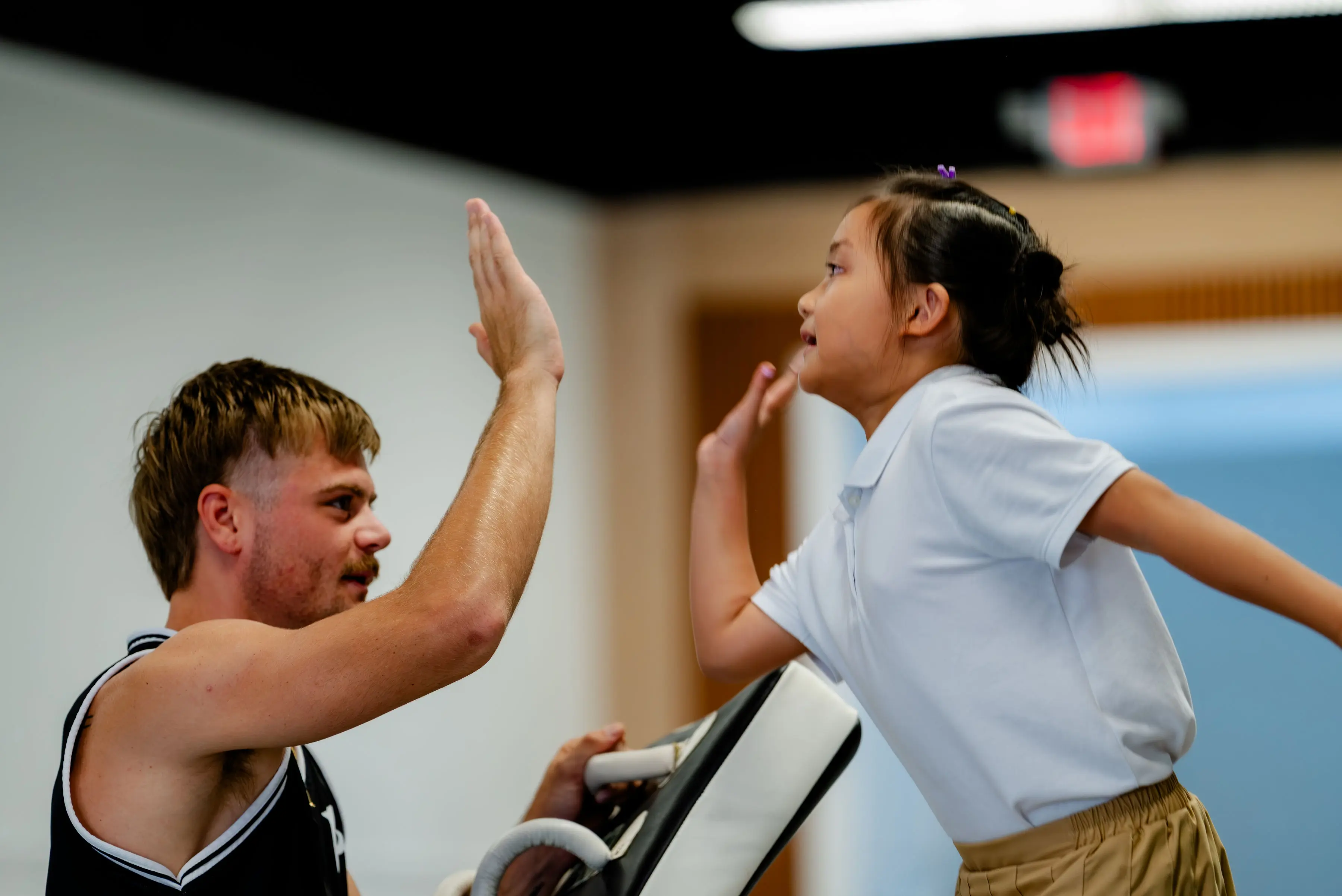 Kids Muay Thai class at RT Beachside: the instructor high-fiving a girl after a round on the pads