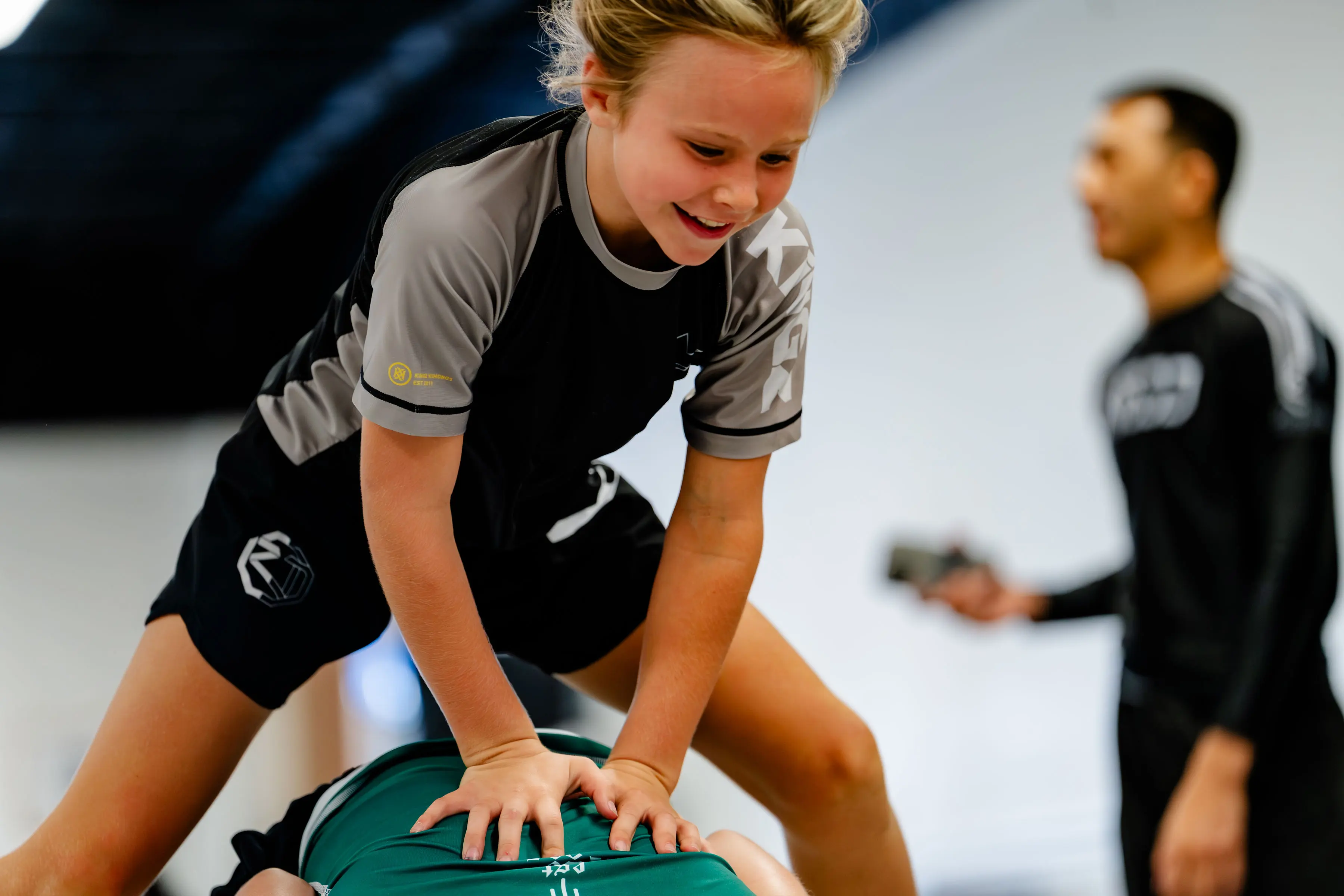 Kids no-gi class at RT Beachside: a girl laughing while pinning her training partner on the mats