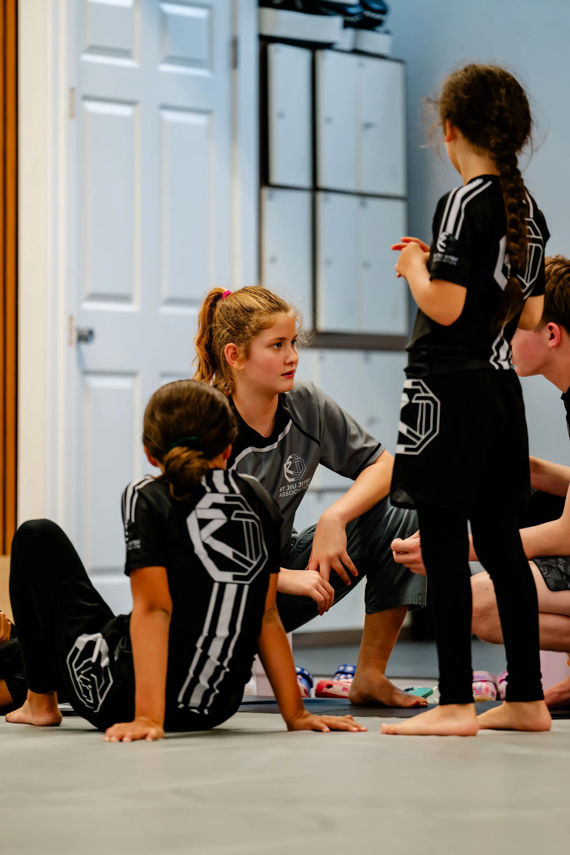Teens no-gi class at RT Beachside: students in black rash guards sitting on the mats, listening to the instructor